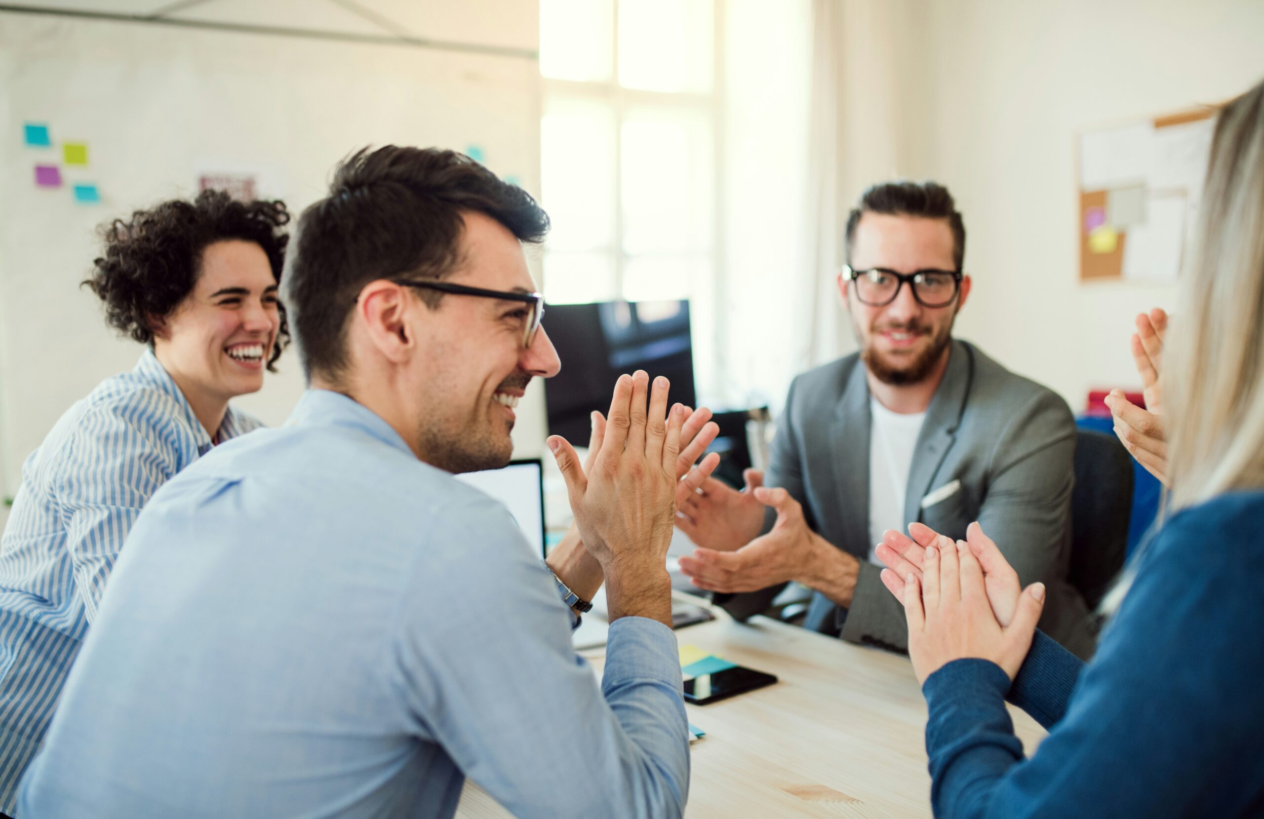 A professional team sitting together at a desk, clapping and celebrating a successful business achievement.