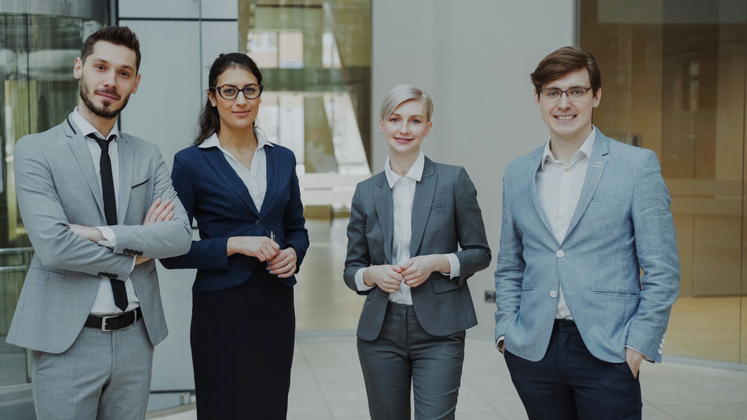 A group of four business professionals standing together in a modern office.